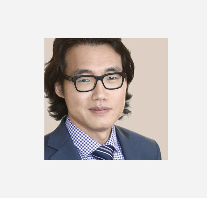 Man wearing glasses and a suit with a checkered shirt on a plain background